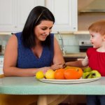 A_photo_of_a_small_child_with_black_hair_sitting_on_a_chair_to_the_left_of_a_kitchen_table_an...jpeg